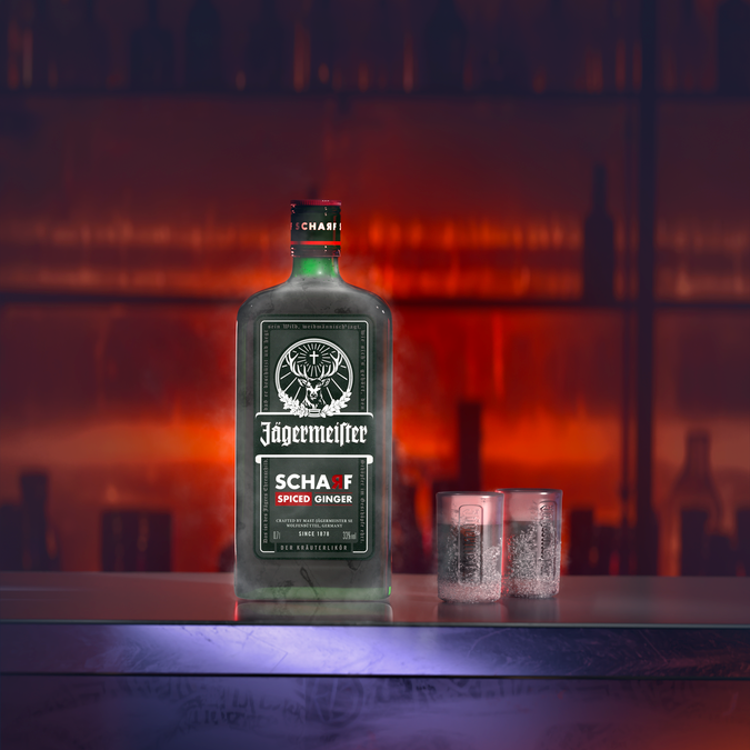 A bottle of Jägermeister Scharf stands on a bar counter with two small glasses beside it, set against a blurred warm red-orange bar interior.