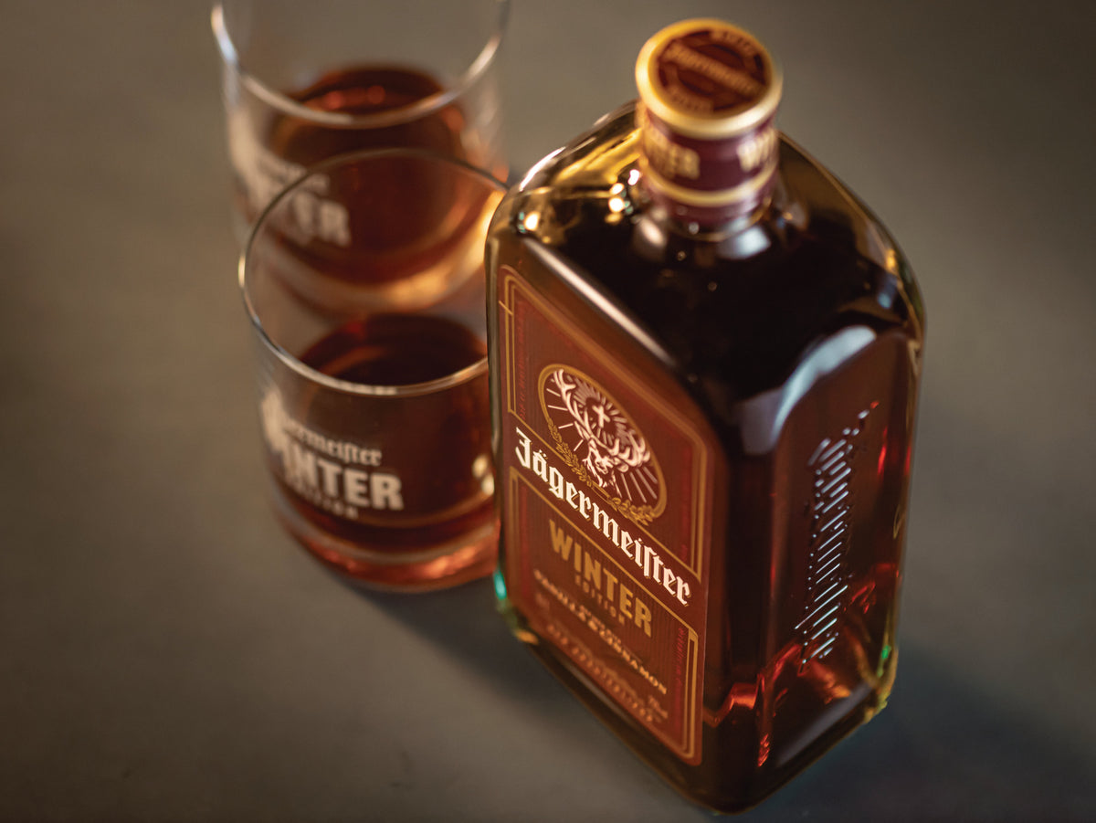A bottle of Jägermeister Winter with two matching glasses filled with the amber liquid, arranged on a dark surface.