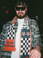 Kockás kabátot viselő személy Jägermeister Racing sállal, napszemüveggel és sapkával.