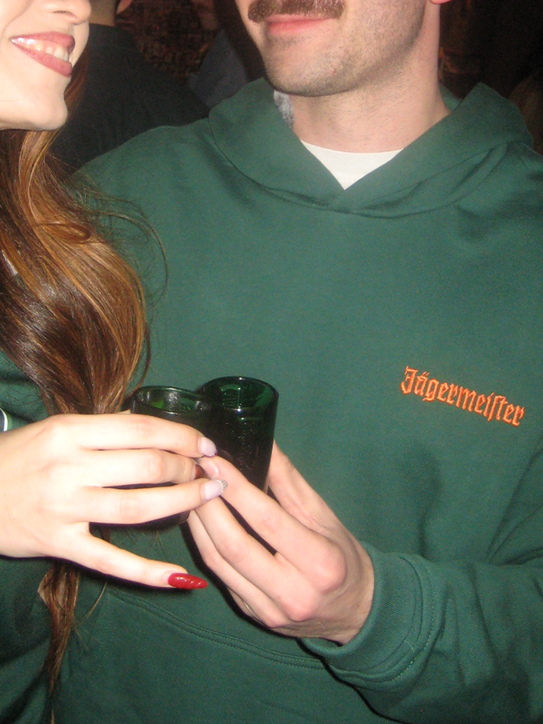 Zöld Jägermeister kapucnis pulóver, narancssárga Jägermeister logóval a mellkason.