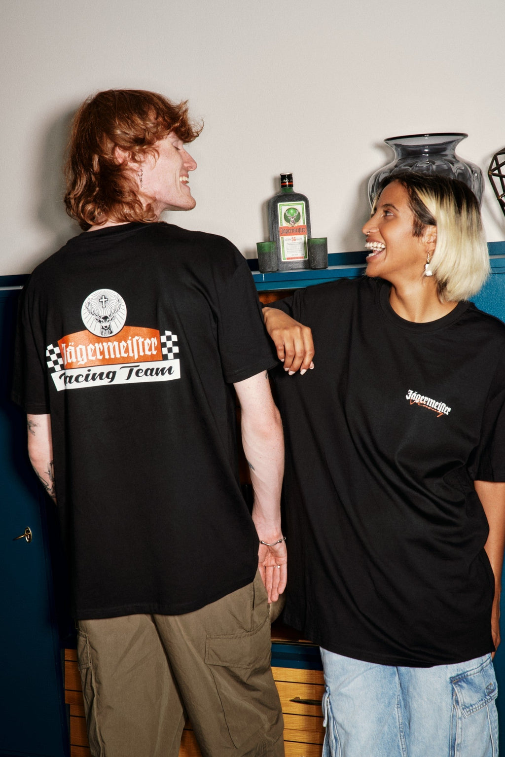 Két ember fekete Jägermeister racing pólóban, logóval és szöveggel, közel állva egymáshoz.
