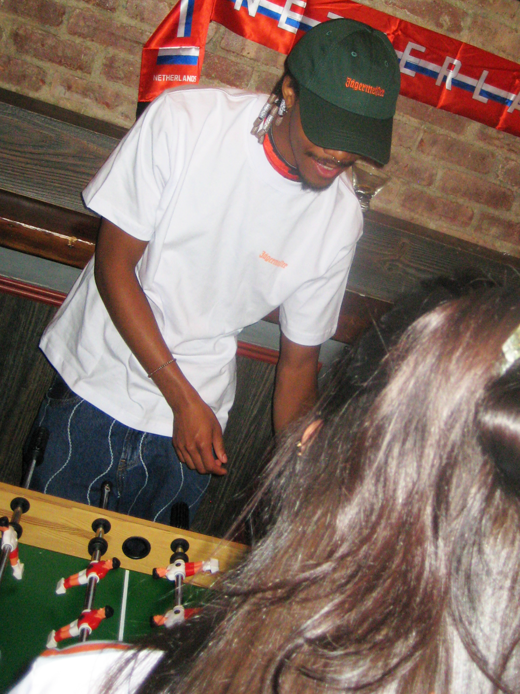 Person playing table football with a brick wall and red and white banner in the background.