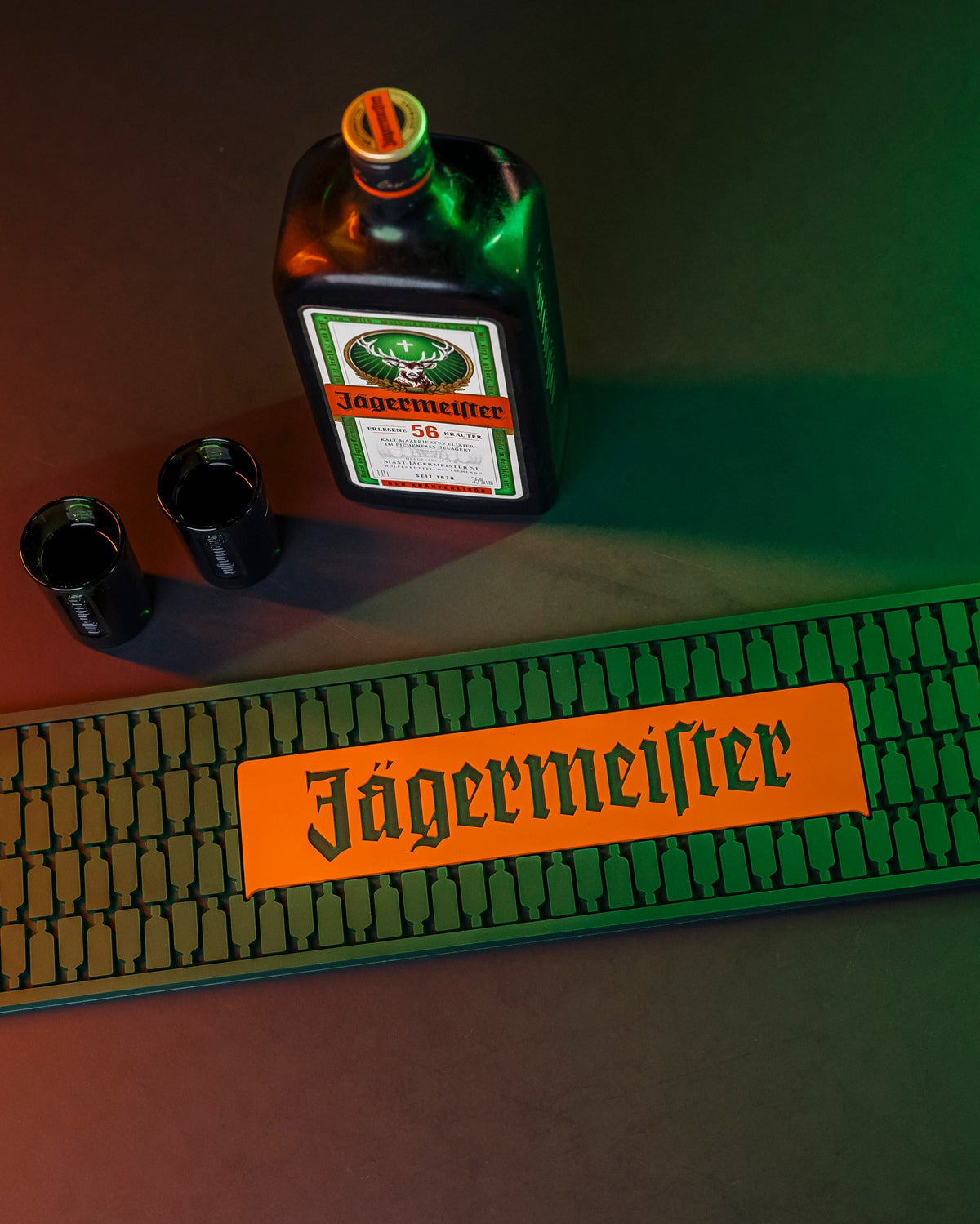 Jägermeifter palack, két shot pohár és bárszőnyeg sötét felületen