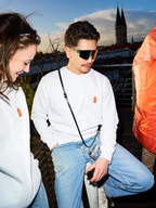 Két ember fehér Jägermeister pulóvert és Jägermeister gyorsszemüveget visel egy tetőteraszon, a háttérben templomtoronnyal és városképpel.