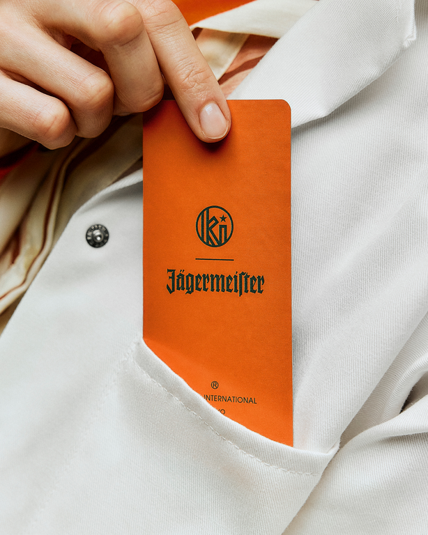 Jägermeister és Kuumba felirat narancssárga illatpapíron, amelyet egy kéz tart fehér köpeny háttere előtt