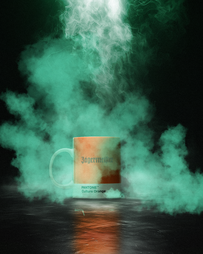 Bögre „Jagermeister” és „Pantone Culture Orange” felirattal, színes füsttel körülvéve, sötét háttéren