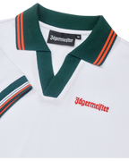 Fehér pólóruha közelről, zöld gallérral és narancssárga részletekkel, Jägermeister-márkajelzéssel.