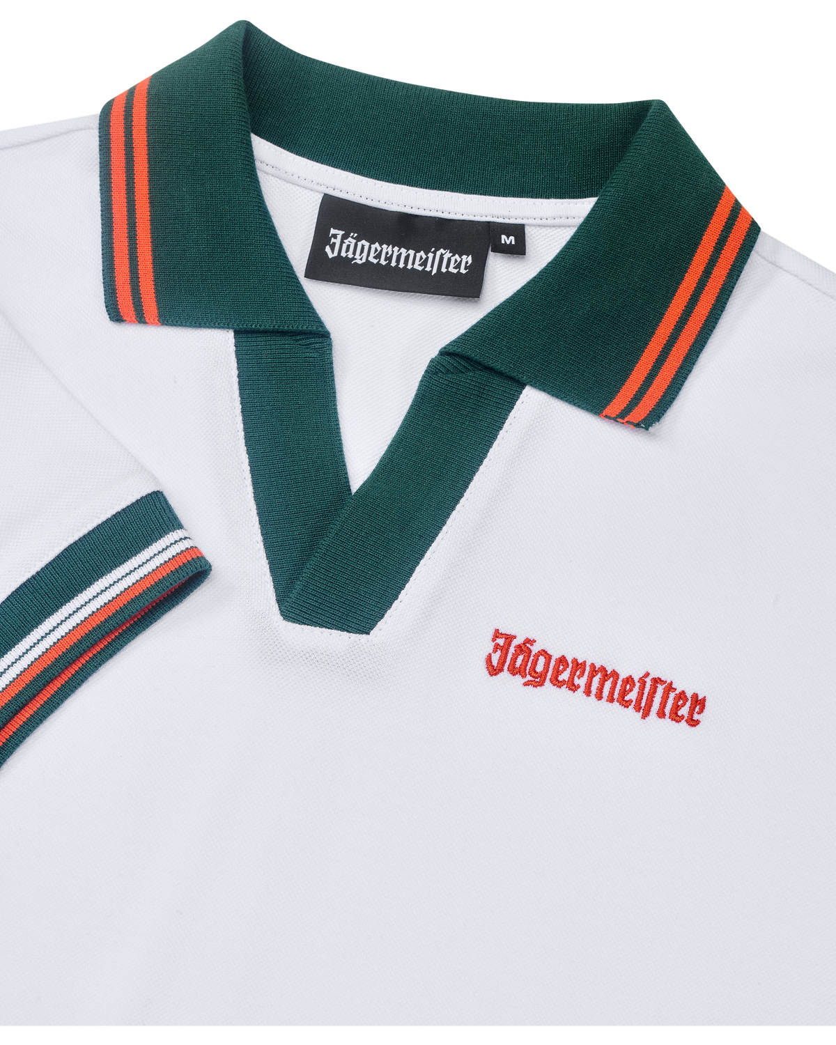 Fehér pólóruha közelről, zöld gallérral és narancssárga részletekkel, Jägermeister-márkajelzéssel.