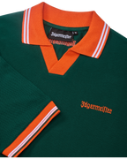 Zöld Jägermeister póló narancssárga gallérral és szegéllyel, Jägermeister-márkajelzéssel.