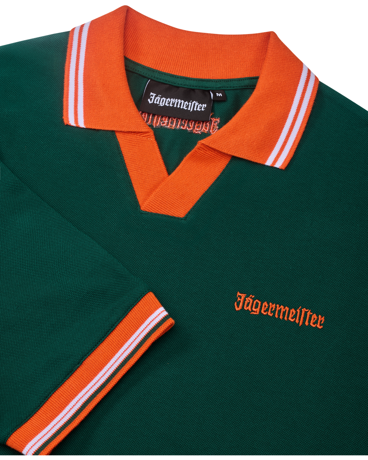 Zöld Jägermeister póló narancssárga gallérral és szegéllyel, Jägermeister-márkajelzéssel.
