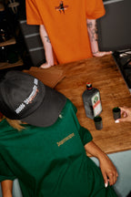 Person wearing a green 'Jägermeister' shirt and black cap Jägermeister Racing Cap sitting at a table with Jägermeister products on it.
