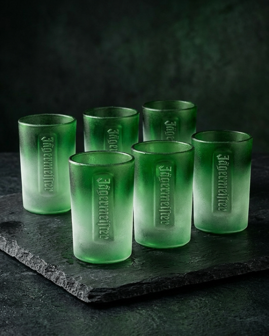 Hat darab zöld shot pohár készlete dombornyomott Jägermeister felirattal egy sötét felületen