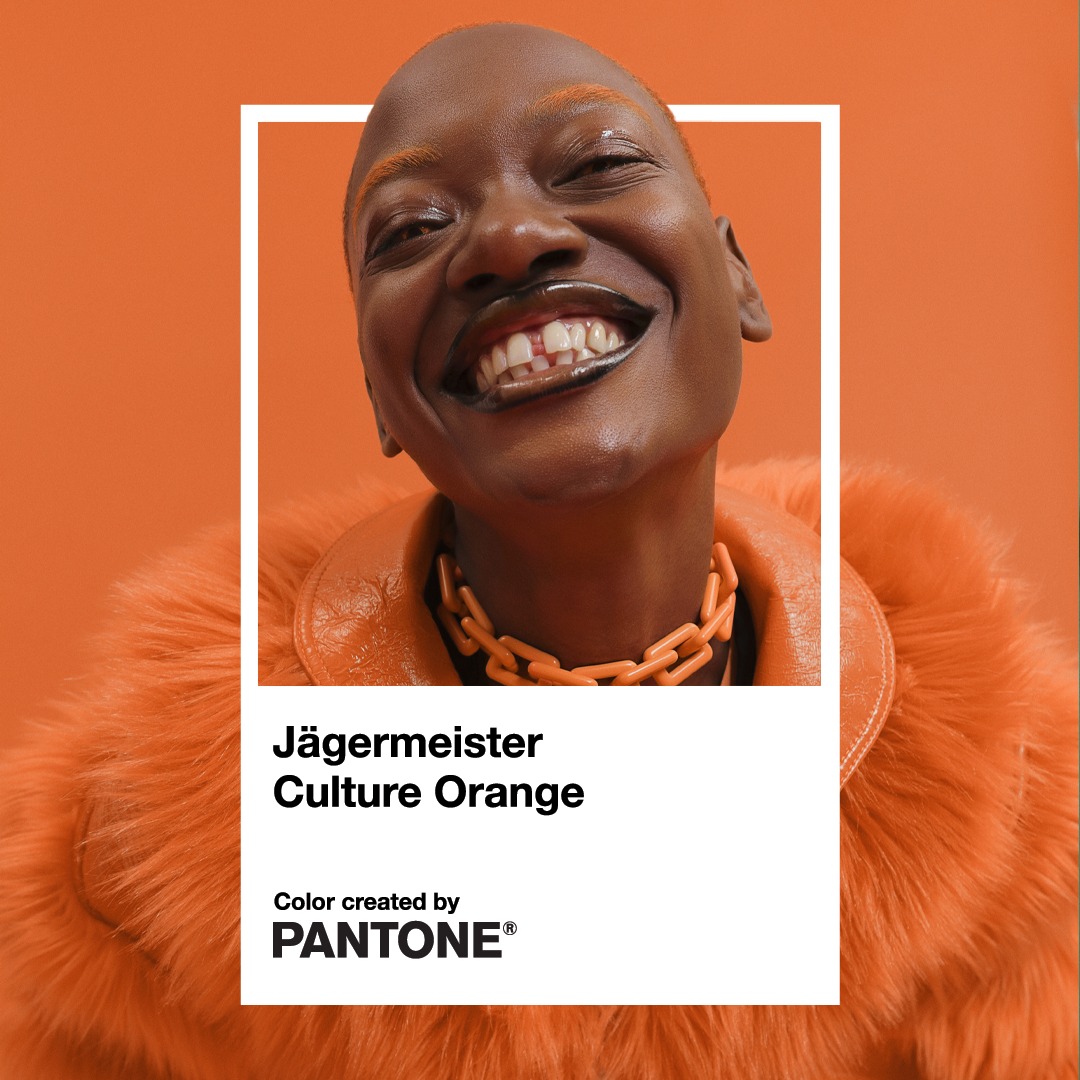 A smiling person in a bright orange fur-like coat and chunky orange chain necklace against a solid orange background, with a white frame and text reading 'Jägermeister Culture Orange' and 'Color created by PANTONE'.
