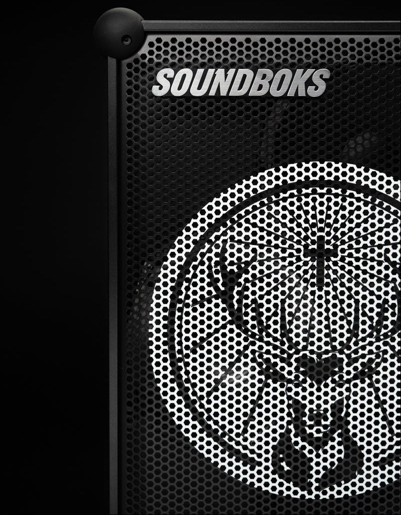 Close-up of a black Soundboks speaker grille with a white deer head logo and the brand name SOUNDBOKS in white text, set against a solid black background.