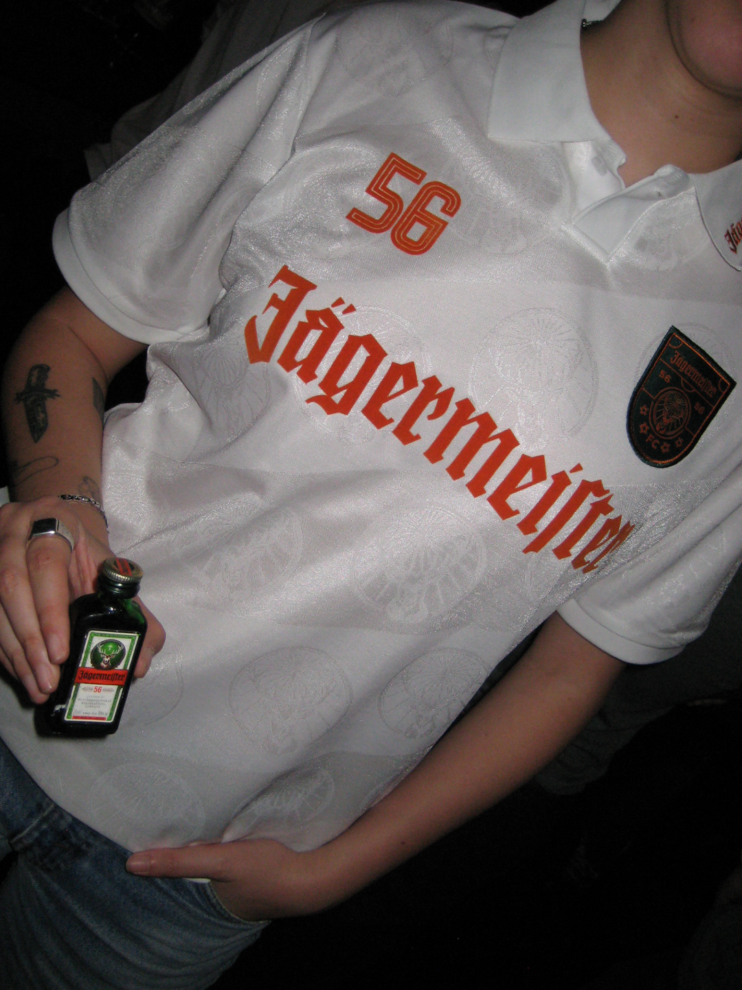 Person wearing a white jersey with 'Jägermeister' branding, holding a Jägermeister Mini.